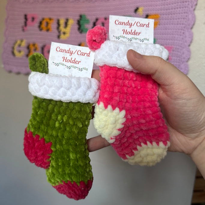 Two small crocheted stockings with a card holder feature, held by a hand against a blurred background.